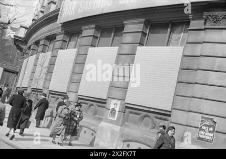 PRECAUZIONI PER BLACKOUT E AIR RAID A LONDRA, INGHILTERRA, 1941 - le finestre di questo grande edificio arrotondato (probabilmente Westminster City Hall su Charing Cross Road) sono state murate, sia per oscurare l'edificio, ma anche per evitare che il vetro venga continuamente distrutto da incursioni aeree. Vari manifesti, tra cui una pubblicità per i risparmi di guerra, possono essere visti sull'edificio, e vari membri del pubblico passano davanti mentre fanno affari quotidiani Foto Stock