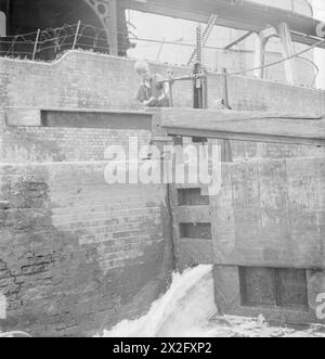 CANALI BRITANNICI IN TEMPO DI GUERRA: TRASPORTI IN GRAN BRETAGNA, 1944 - Un giovane ragazzo, figlio di un barcaiolo del canale, gira la maniglia di una serratura, probabilmente da qualche parte lungo il Regent's Canal. Sta salendo le pale per lasciare che l'acqua dal livello superiore riempia la serratura e solleva le barche Foto Stock