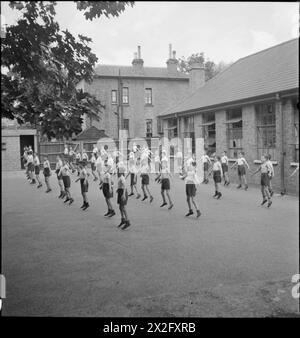 SCUOLA ELEMENTARE CATTOLICA: VITA A St JOSEPH'S, NORWOOD SUPERIORE, 1943 - i bambini fanno salti a forbice come parte della loro classe di palestra nel parco giochi della St Joseph's Elementary School. Secondo la didascalia originale: "I loro canottieri, pantaloncini corti e scarpe sono forniti dal Board of Education" Foto Stock