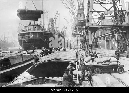 Durante la seconda guerra mondiale, i portuali spostarono merci importate ed esportate utilizzando mani, veicoli e gru tra navi mercantili e chiatte fluviali in un cantiere navale britannico, probabilmente sulla costa occidentale. Foto Stock