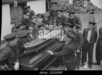 PRESSO L'ISTITUTO DI ADDESTRAMENTO DELLA MARINA MERCANTILE HMS GORDON. GIUGNO 1941, HMS GORDON, GRAVESEND. QUESTI UOMINI FIRMARONO PER IL SERVIZIO PRESSO LA ROYAL NAVY E GLI FU CHIESTO DI FARE VOLONTARIATO PER IL SERVIZIO MERCANTILE. - L'istruttore che spiega parti di una nave mercantile per mezzo di un modello alla sua classe Foto Stock