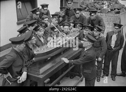 PRESSO L'ISTITUTO DI ADDESTRAMENTO DELLA MARINA MERCANTILE HMS GORDON. GIUGNO 1941, HMS GORDON, GRAVESEND. QUESTI UOMINI FIRMARONO PER IL SERVIZIO PRESSO LA ROYAL NAVY E GLI FU CHIESTO DI FARE VOLONTARIATO PER IL SERVIZIO MERCANTILE. - L'istruttore che spiega parti di una nave mercantile per mezzo di un modello alla sua classe Foto Stock