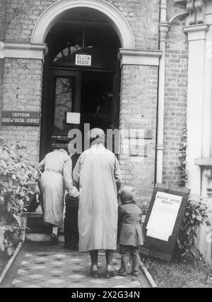 IL LAVORO DEL CITIZENS' ADVICE BUREAU, ELDON HOUSE, CROYDON, INGHILTERRA, 1940 - due donne e i loro figli arrivano al Citizens' Advice Bureau per chiedere un aumento delle indennità Foto Stock