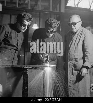 I WRENS SI ALLENANO PER UN NUOVO LAVORO: FORMAZIONE PER MECCANICI NAVALI DEL SERVIZIO NAVALE REALE FEMMINILE, INGHILTERRA, Regno Unito, 1943 - Sparks vola come membro del WRNS taglia una barra di ferro utilizzando una torcia ossiacetilene come parte del suo addestramento per diventare un meccanico di nave (LC), probabilmente presso il Slough Government Training Centre. È osservata dal suo istruttore e da un altro Wren. Indossano tutti occhiali protettivi Foto Stock