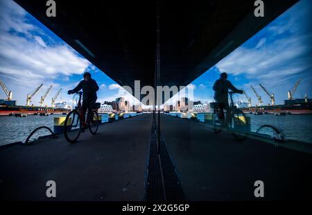 22 aprile 2024, Meclemburgo-Pomerania Occidentale, Wismar: Un ciclista passa davanti al vetro del centro tecnologico del porto marittimo e si riflette nelle finestre. Il clima primaverile nella Germania settentrionale è attualmente freddo e talvolta ventoso. Foto: Jens Büttner/dpa Foto Stock