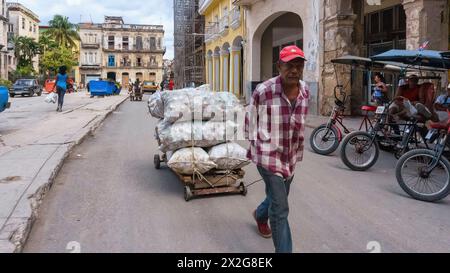 Uomo cubano che tira un carrello rustico pieno di sacchi in alluminio, l'Avana, Cuba Foto Stock