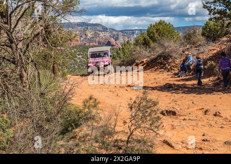 La jeep rosa della Pink Jeep Tours passa per gli escursionisti che riposano lungo la strada accidentata utilizzata dai veicoli fuoristrada a Sedona, Arizona Foto Stock