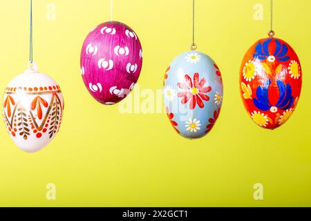 Uova di pasqua dipinte a mano appese su sfondo giallo Foto Stock