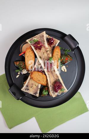 vista dall'alto delicata, midollo osseo cotto con crostini, erbe e spezie su un piatto nero. Foto Stock