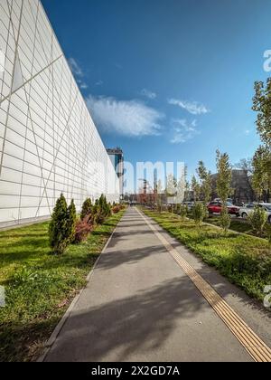 Struttura architettonica contemporanea dal design geometrico, circondata da vegetazione lussureggiante, adagiata su uno sfondo di cielo azzurro. Foto Stock