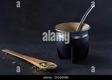 black mate con bombilla su sfondo nero e un cucchiaio di legno con yerba mate. copia spazio. tradizionale bevanda calda argentina Foto Stock