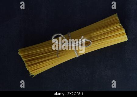 Vista dall'alto degli spaghetti secchi legati con un cordoncino rustico su sfondo nero. Copia spazio Foto Stock