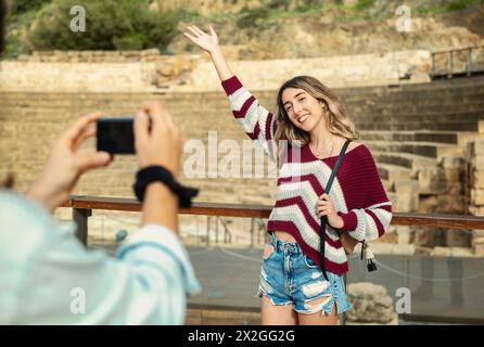 Due amici turisti si posano di fronte a un monumento a Malaga, mentre uno fotografa l'altro sorridendo e sollevando un braccio. Foto Stock