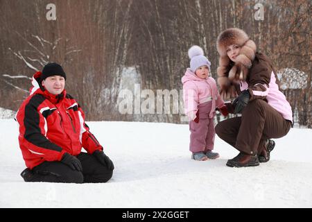 figlia piccola con madre, padre seduto sulla neve in inverno, concentrata su ragazza Foto Stock