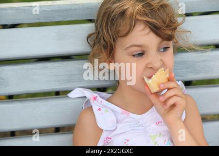 La bambina si siede sulla panchina e mangia del gelato Foto Stock