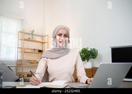 Giovane donna d'affari musulmana contabile che lavora con documenti finanziari, calcola le tasse. Donna musulmana libera professionista lavora a casa Foto Stock