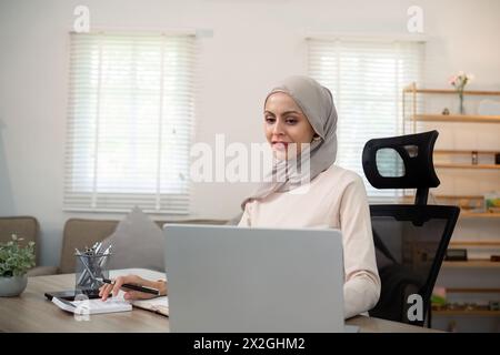 Giovane donna d'affari musulmana contabile che lavora con documenti finanziari, calcola le tasse. Donna musulmana libera professionista lavora a casa Foto Stock