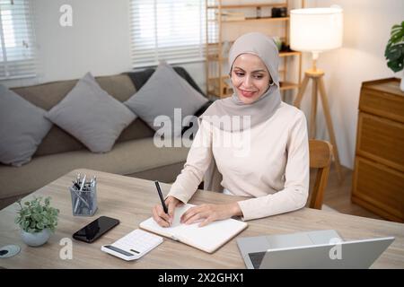 La giovane donna d'affari musulmana calcola la finanza del budget. La donna musulmana commercialista usa calcolatrice digitando laptop contando le bollette dei prestiti fiscali online Foto Stock