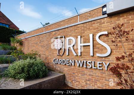 Il logo RHS e il cartello con il nome all'ingresso del RHS Garden, Wisley, Surrey, Inghilterra sud-orientale in primavera Foto Stock