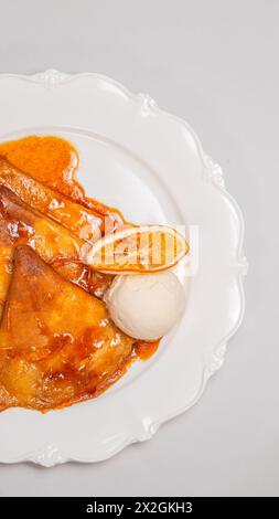 Un delizioso dessert di crepe condite con salsa all'arancia e una pallina di gelato alla vaniglia, isolato su sfondo bianco. Foto Stock
