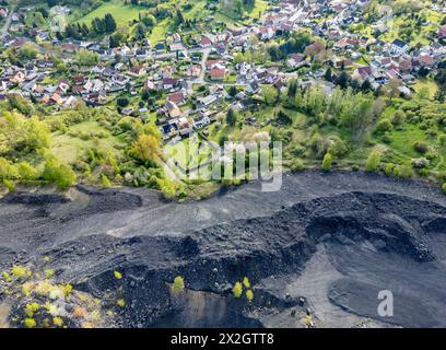 Hergisdorf, Germania. 18 aprile 2024. Un cumulo di scorie dei tempi dell'estrazione del rame domina il paesaggio accanto alla piccola città. Tra il 2020 e il 2040, si prevede che la popolazione di Mansfeld-Südharz diminuirà del 21,1%. Previsioni simili sono fatte per gli altri stati della Germania orientale. Allo stesso tempo, la percentuale di anziani è in aumento. I distretti stanno facendo del loro meglio per combattere questa situazione. (Vista aerea con drone) credito: Jan Woitas/dpa/Alamy Live News Foto Stock