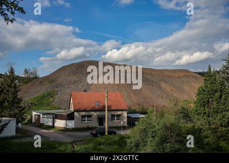 Kreisfeld, Germania. 18 aprile 2024. Un mucchio di scorie dei tempi dell'estrazione del rame domina il paesaggio dietro una piccola casa in questo piccolo villaggio. Secondo le previsioni, la popolazione di Mansfeld-Südharz è destinata a ridursi del 21,1% tra il 2020 e il 2040. Previsioni simili sono fatte per gli altri stati della Germania orientale. Allo stesso tempo, la percentuale di anziani è in aumento. I distretti stanno facendo del loro meglio per combattere questa situazione. Crediti: Jan Woitas/dpa/Alamy Live News Foto Stock