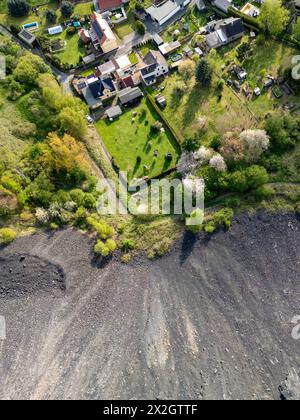 Hergisdorf, Germania. 18 aprile 2024. Un cumulo di scorie dei tempi dell'estrazione del rame domina il paesaggio accanto alla piccola città. Tra il 2020 e il 2040, si prevede che la popolazione di Mansfeld-Südharz diminuirà del 21,1%. Previsioni simili sono fatte per gli altri stati della Germania orientale. Allo stesso tempo, la percentuale di anziani è in aumento. I distretti stanno facendo del loro meglio per combattere questa situazione. (Vista aerea con drone) credito: Jan Woitas/dpa/Alamy Live News Foto Stock