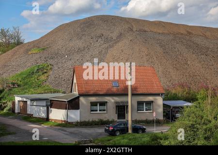 Kreisfeld, Germania. 18 aprile 2024. Un mucchio di scorie dei tempi dell'estrazione del rame domina il paesaggio dietro una piccola casa in questo piccolo villaggio. Secondo le previsioni, la popolazione di Mansfeld-Südharz è destinata a ridursi del 21,1% tra il 2020 e il 2040. Previsioni simili sono fatte per gli altri stati della Germania orientale. Allo stesso tempo, la percentuale di anziani è in aumento. I distretti stanno facendo del loro meglio per combattere questa situazione. Crediti: Jan Woitas/dpa/Alamy Live News Foto Stock