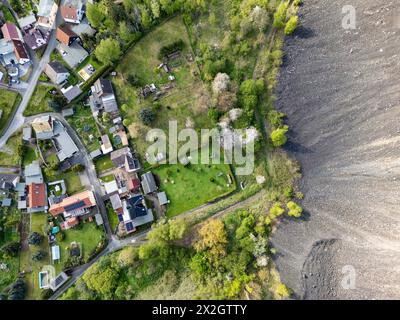 Hergisdorf, Germania. 18 aprile 2024. Un cumulo di scorie dei tempi dell'estrazione del rame domina il paesaggio accanto alla piccola città. Tra il 2020 e il 2040, si prevede che la popolazione di Mansfeld-Südharz diminuirà del 21,1%. Previsioni simili sono fatte per gli altri stati della Germania orientale. Allo stesso tempo, la percentuale di anziani è in aumento. I distretti stanno facendo del loro meglio per combattere questa situazione. (Vista aerea con drone) credito: Jan Woitas/dpa/Alamy Live News Foto Stock