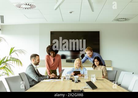 Un gruppo di professionisti si è riunito intorno a un notebook, condividendo idee in un ambiente luminoso. Foto Stock