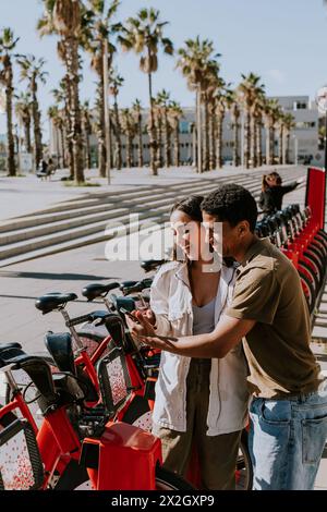 Coppia giovane che si gode una giornata di vento scegliendo le biciclette da una stazione di noleggio a Barcellona. Foto Stock