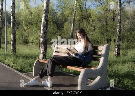 Ritratto di una bella ragazza con un libro. Sta succedendo da qualche parte nel parco. Primo piano. Foto Stock