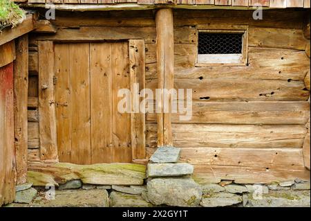 Pareti di fienile in legno battute dal tempo con una porta solida e gradino in pietra. Foto Stock