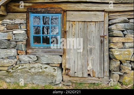 Una vista ravvicinata di una vecchia capanna in legno con fondamenta in pietra, porta e finestra intemperie. Foto Stock