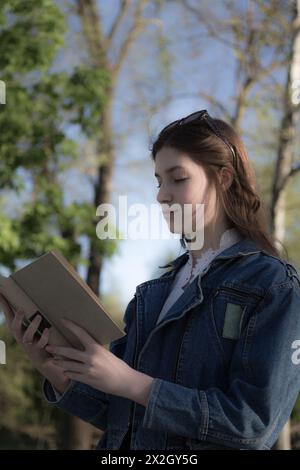 Ritratto di una bella ragazza con un libro. Sta succedendo da qualche parte nel parco. Primo piano. Foto Stock