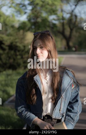 Ritratto di una bella ragazza con un libro. Sta succedendo da qualche parte nel parco. Primo piano. Foto Stock