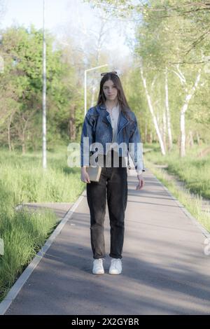 Ritratto di una bella ragazza con un libro. Sta succedendo da qualche parte nel parco. Primo piano. Foto Stock