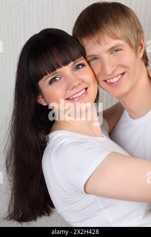 Giovane uomo e donna vestiti con camicie bianche abbracciano su sfondo bianco lavorato a maglia Foto Stock