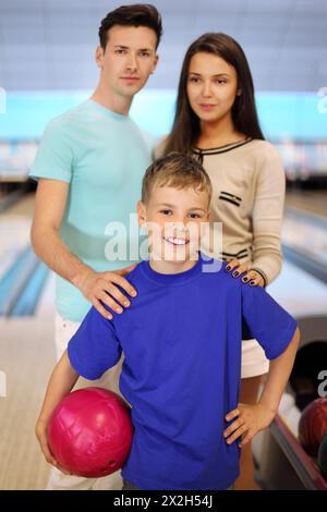 Il giovane padre e la madre tengono le spalle al figlio nel club di bowling; concentrarsi sul ragazzo; profondità di campo bassa Foto Stock