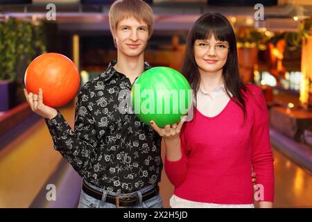 moglie e marito felici con le palle in piedi nel club di bowling e guardare la macchina fotografica Foto Stock