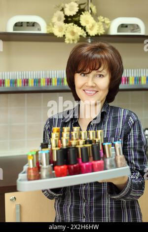 Una donna sorridente tiene uno smalto colorato sul piedistallo nel salone di bellezza; vista verticale Foto Stock