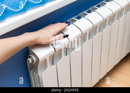 uomo che controlla la temperatura di un radiatore di riscaldamento. una donna tiene la mano su un radiatore di riscaldamento controllandone la temperatura. la mano tocca il radiatore Foto Stock