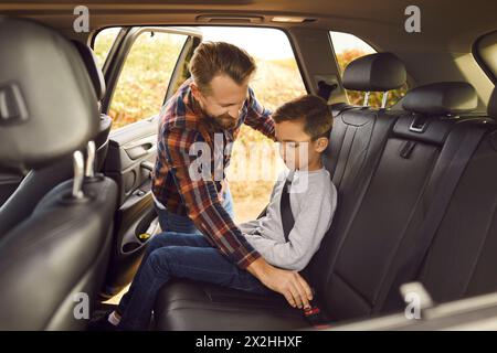 Il padre premuroso sta allacciando la cintura di sicurezza per suo figlio sul sedile posteriore di un'auto di famiglia. Foto Stock