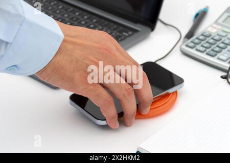 Mano di un uomo d'affari che carica il suo smartphone con un caricabatterie wireless in ufficio Foto Stock