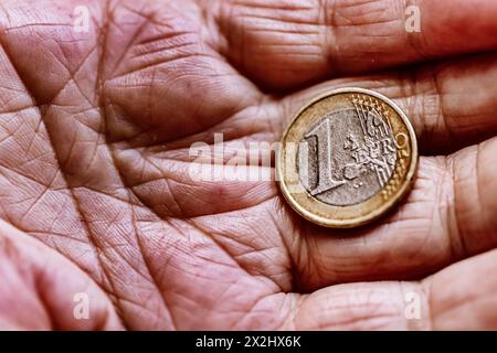 Una moneta in euro nella mano rugosa di un anziano cittadino, che simboleggia la povertà e la povertà nella vecchiaia Foto Stock