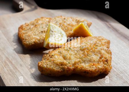 Filetti di merluzzo in pastella tempura ricoperti di erbe aromatiche e limone con una fetta di limone. Su un tagliere di legno. Foto Stock