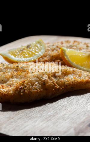 Filetti di merluzzo in pastella tempura ricoperti di erbe aromatiche e limone con una fetta di limone. Su un tagliere di legno. Foto Stock