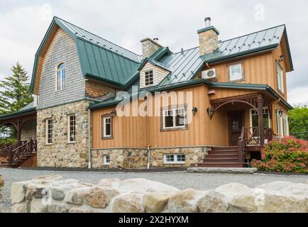 Facciata di una vecchia casa in pietra di campo in stile cottage canadese del 1826 con rivestimento verticale in legno, tegole di cedro e tetto in lamiera di cuciture verdi Foto Stock