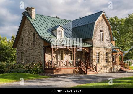 Facciata di una vecchia casa in pietra di campo in stile cottage canadese del 1826 con rivestimento verticale in legno, tegole di cedro e tetto in lamiera di cuciture verdi Foto Stock