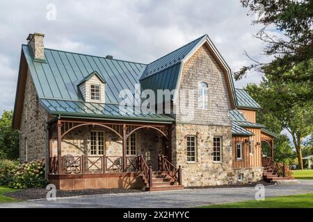 Facciata di una vecchia casa in pietra di campo in stile cottage canadese del 1826 con rivestimento verticale in legno, tegole di cedro e tetto in lamiera di cuciture verdi Foto Stock